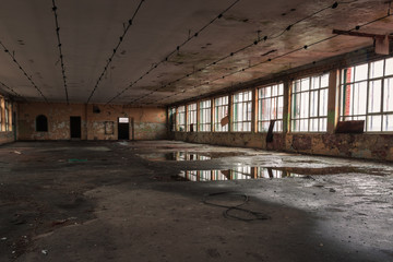 Shabby interior with big windows and reflections in  the puddles on the floor inside the abandoned factory building