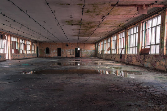 Shabby interior with big windows and reflections in  the puddles on the floor inside the abandoned factory building