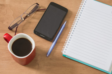 Blank notebook with cell phone and cup of coffee on wooden background.