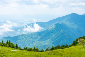 Obraz premium Slovenia mountains near the Kamnik city on Velika Planina pasture land. View of mountains with white clouds and blue sky, mist in the hill. Beautiful and tranquil nature, fresh grass