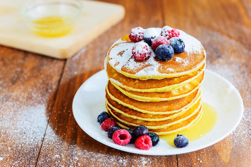 American pancakes with berries, honey and powdered sugar on a wooden table
