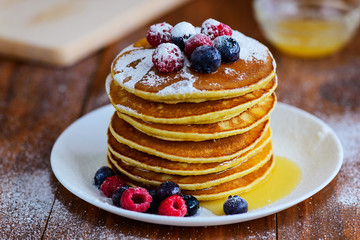 American pancakes with berries, honey and powdered sugar on a wooden table