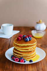 American pancakes with berries and honey on a wooden table