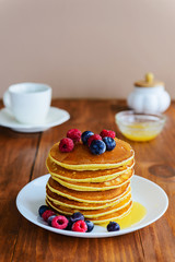 American pancakes with berries and honey on a wooden table