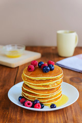 American pancakes with berries and honey on a wooden table