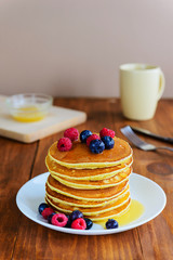 American pancakes with berries and honey on a wooden table