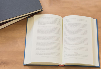 Fototapeta premium Open book with pile of closed books on wooden background.