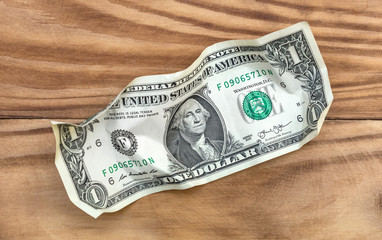 Crumpled one dollar bill on wooden background. Top view.