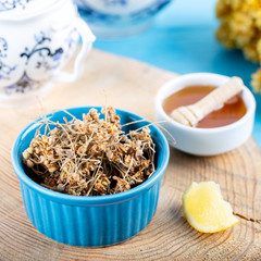 Dried linden flowers in bowl with honey and lemon on wooden background