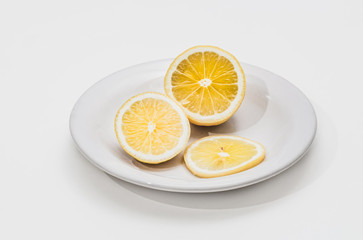 A fresh yellow lemon sliced into three slices is on a white plate on a white background