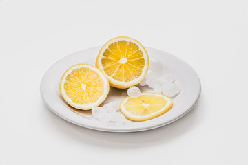 A fresh yellow lemon sliced into three slices is on a white plate with white crystals of sugar candies on a white background