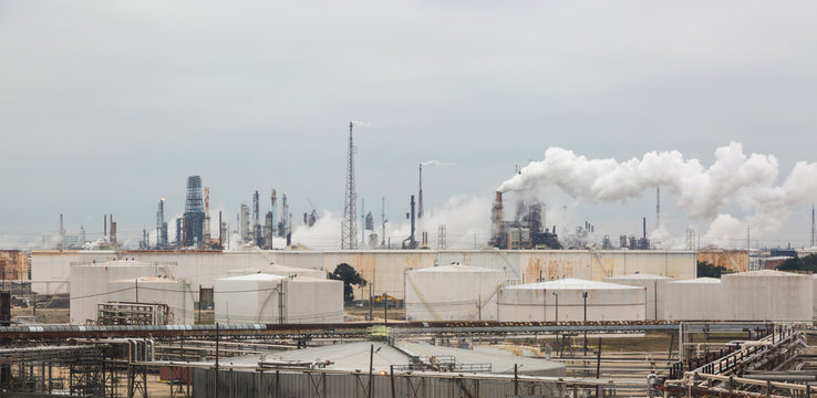 Panorama of an oil refinery with smoky smokes under a gray cloudy sky.