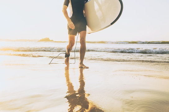 Surfer man with long board walking out fro sea waves on sunny ocean beach. Active vacation spending time concept image.