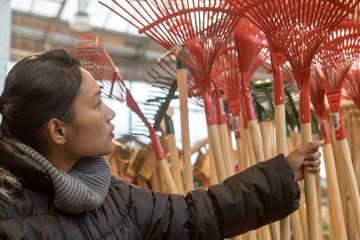 Purchase of garden supplies in a department store. Young woman choosing a rake in a shop.