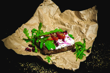 Breakfast bread toast with curd spread, tomatoes, pepper, decorated by rucola served on rustic paper with black background