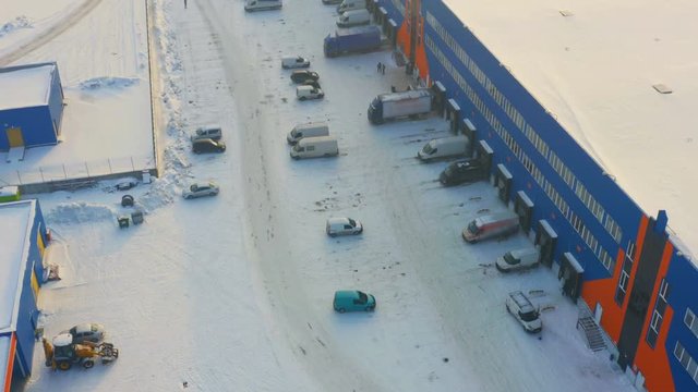 Aerial view of a of warehouse logistics hub with semi-trailers trucks and commercial vehicles on a snowy parking lot on a winter day