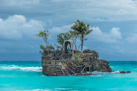 Willys Rock - an oddly shaped volcanic formation with a statue of the Blessed Virgin Mary at azure sea cloudy day in Bocaray, Philippine Islands.