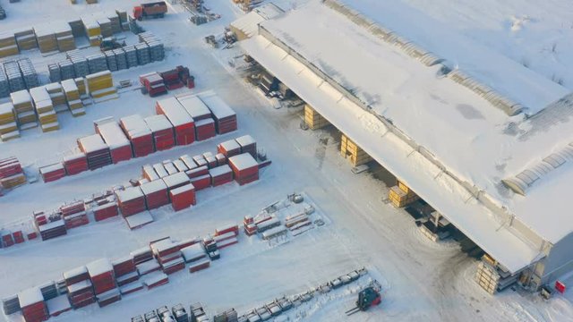 Aerial view of a storage yard and warehouse of a modern bright building and structural materials on a winter snowy day