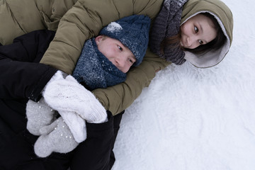 A girl with a guy wallowing in the snow and hugging each other.