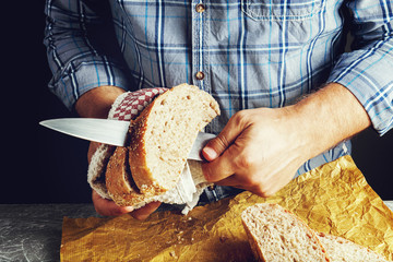 A man cuts freshly baked whole-wheat bran bread with a sharp knife