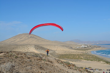 Skydiver flying over the Fuerteventura mountain with red parachute down the wind