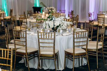 Wedding dinner table decor. Indian reception or banquet. Pastel and white colors. Long tables decorated with white flowers and golden cutlery.