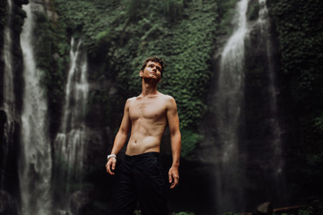 young man muscular and beautiful standing near the waterfall