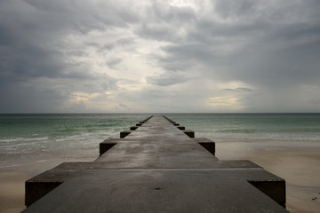 Sandy beach with concrete pier extending into the sea with a cloudy stormy sky on the Gulf Coast in Florida, USA