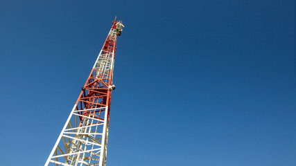 Looking up to small red and white telecommunications tower, communication dishes on top. Abstract technology background, space for text on right.