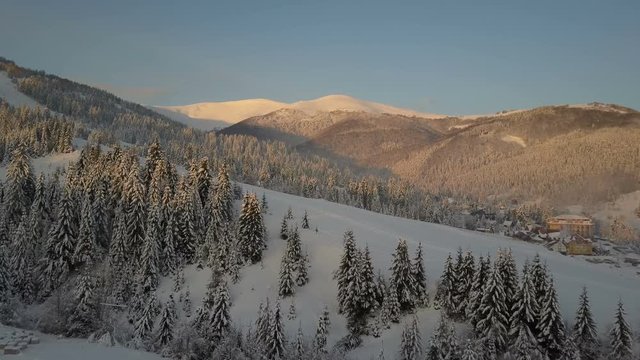 Flight over a village in Carpathian mountains. Bird's eye view of snow-covered houses in mountains. Rural landscape in winter. Carpathian village in the snow from a height.