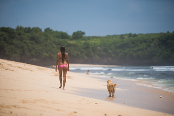 Woman in bikini and dog walking on the sand beach