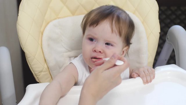 Little baby learns to eat porridge from spoon. Mom introduces kid first feed in diet.