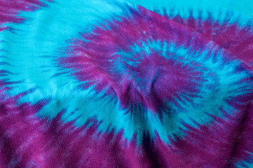 Close up of multi colored tie dyed fabric background showing spiral of pink and purple on aqua blue.