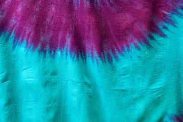 Close up of multi colored tie dyed fabric background showing starburst of pink and purple on aqua...