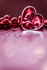 Shining transparent heart and a group of red beads. Perfect Valentine's Day greeting card background. Vertical image in pink tone