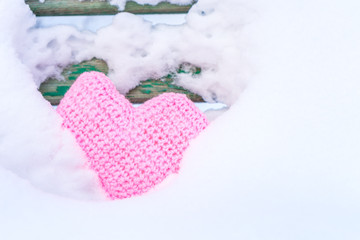 Knitted pink homemade heart on the background of the back of a snow-covered bench