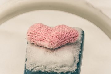 Obraz na płótnie Canvas Homemade knitted pink heart on snow-covered swings