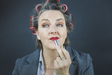 Frau, 40+, im Business Outfit und roten Lockenwicklern im Haar macht sich bereit fürs Büro.