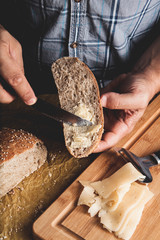 Preparing healthy vegetarian bruschettas on rustic wooden table. Top view on male hands spreading soft cheese on rye wholegrain bread. Making sandwiches for snack