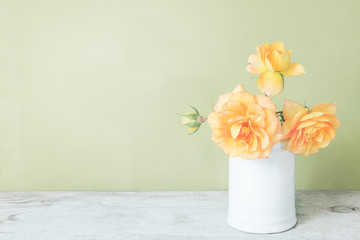 Yellow roses in retro white vase on wood table on green wall with copy space.