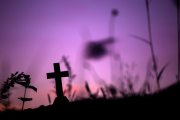 Cross of christian in silhouette on a hill with light sunset background.