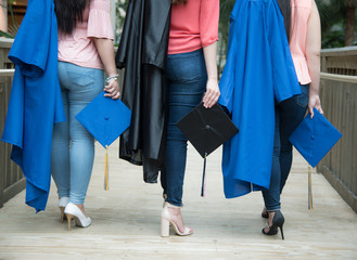 Fototapeta na wymiar Three girl friends holding blue graduation cap and gown view of legs and high heel shoes wearing jeans
