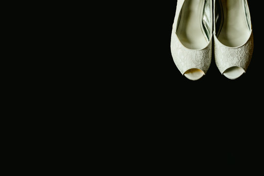 Beautiful white wedding shoes in a corner on isolated black background, copy space.