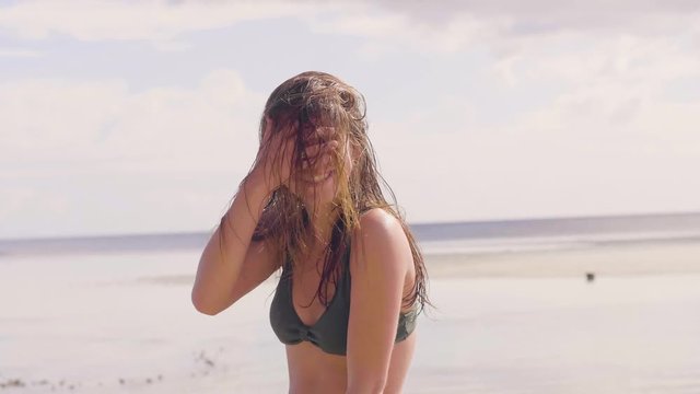 Portrait brunette woman shaking wet hair on sea beach. Cheerful woman with wet long hair shaking head on sea beach landscape. Beautiful girl posing to camera on ocean shore.