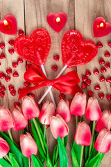 Heart shaped lollipops on wooden background with heart shaped candles lined with tulips flowers. Festive background to the Valentine's day.