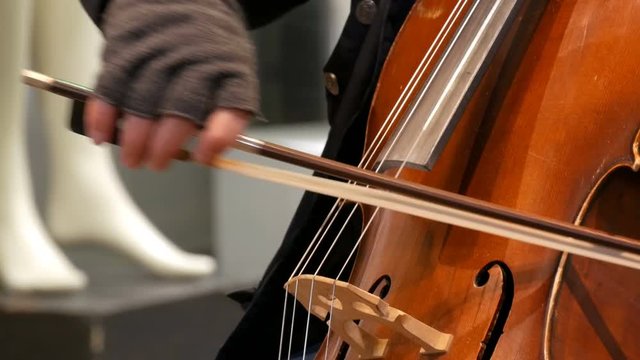Street musician playing the cello close up view. Cellist in gloves gently bows strings