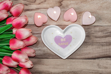 Flowers tulips, a heart-shaped plate and a heart-shaped candle. Festive background to the St. Valentine's Day in pink colors.