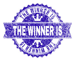 THE WINNER IS rosette stamp overlay with grunge texture. Designed with round rosette, ribbon and small crowns. Blue vector rubber watermark of THE WINNER IS title with grunge texture.