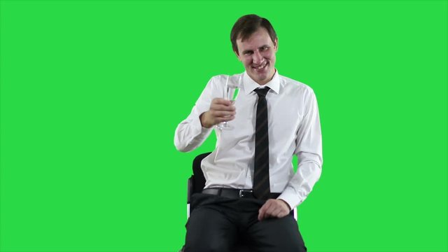 Young modern white-collar worker proposes a toast against a green screen. Portrait of young successful businessman in a shirt sitting and holding in hand wineglass. 