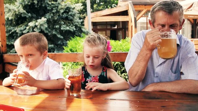 Kids with grandfather in a summer cafe. Tasty dinner with grandfather. Grandpa drinks beer, children have a delicious juice.
